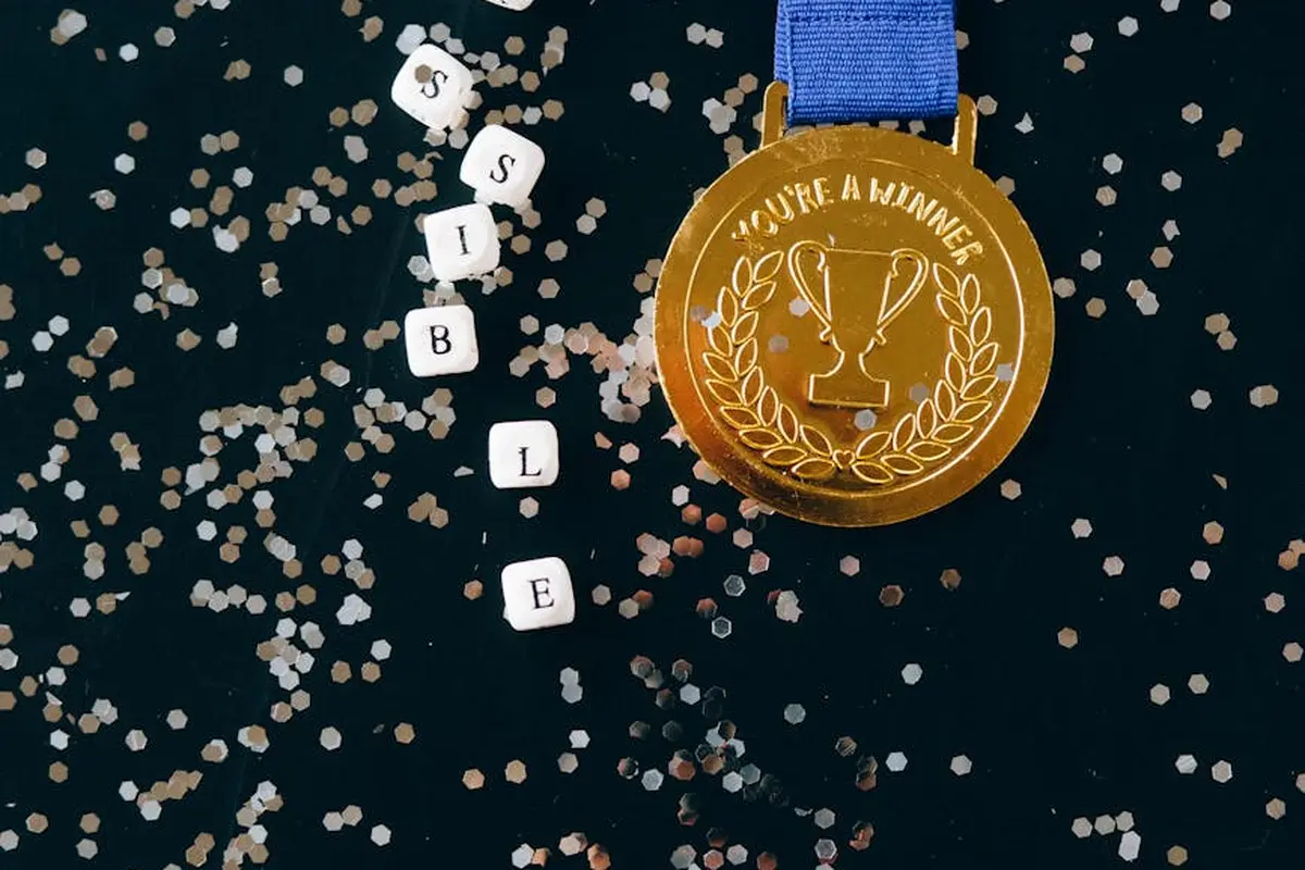 Gold medal with a blue ribbon on a dark surface, surrounded by scattered confetti.