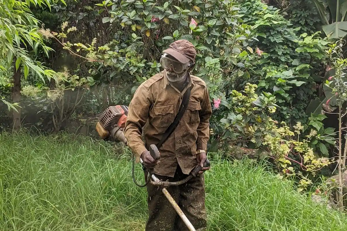 Person in brown protective suit with gloves and a respirator mask operating a yard maintenance tool in a grassy garden.