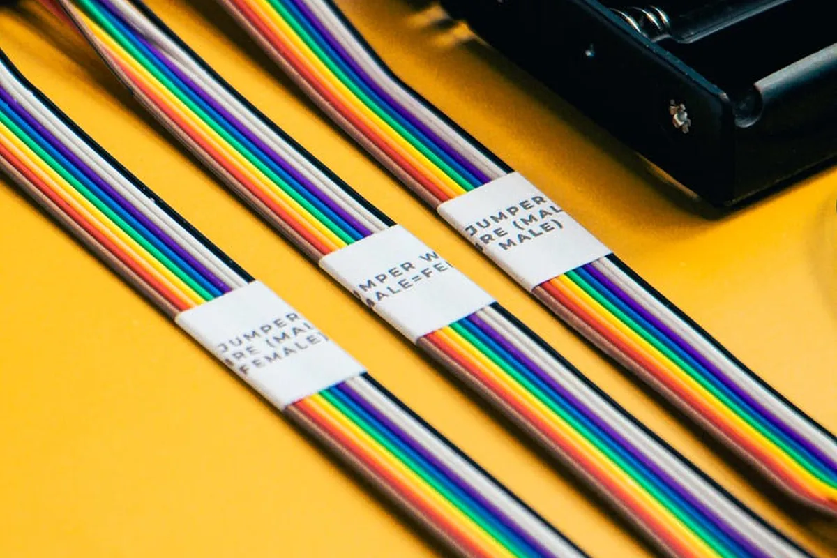 Close-up of color-coded electrical wires with white label tags on a bright yellow surface.