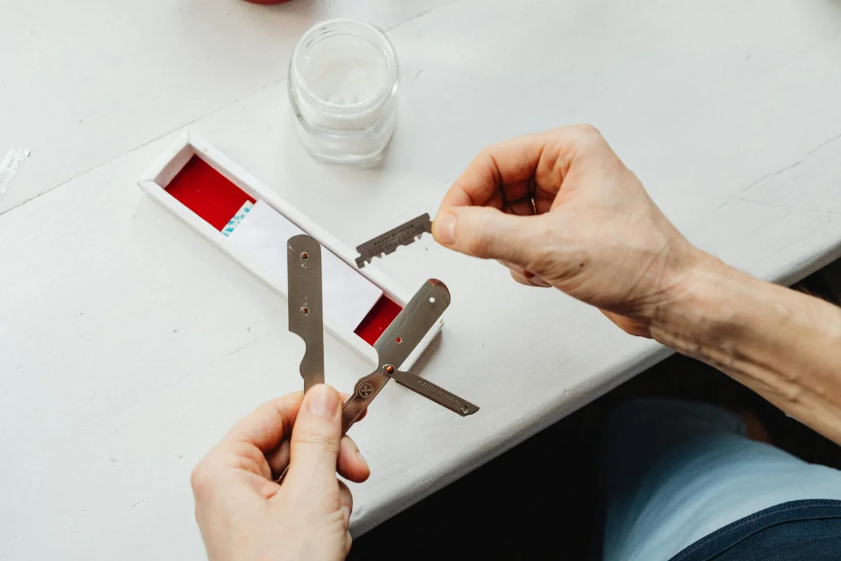 Hands holding lawn mower blades and a blade sharpener/tool over a clean white work surface