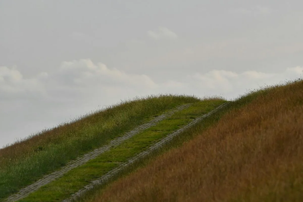 Grassy steep hillside with a narrow dirt path running along the slope, illustrating erosion-prone terrain.