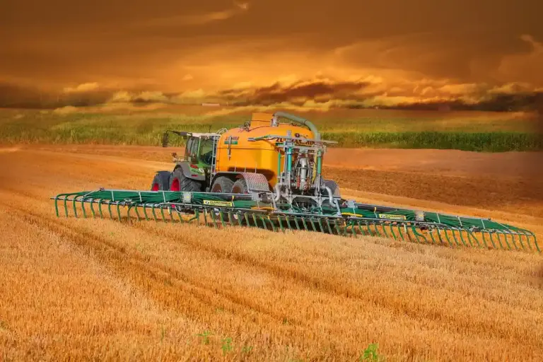 A yellow combine harvester in a golden wheat field at sunset, with a dramatic orange sky.