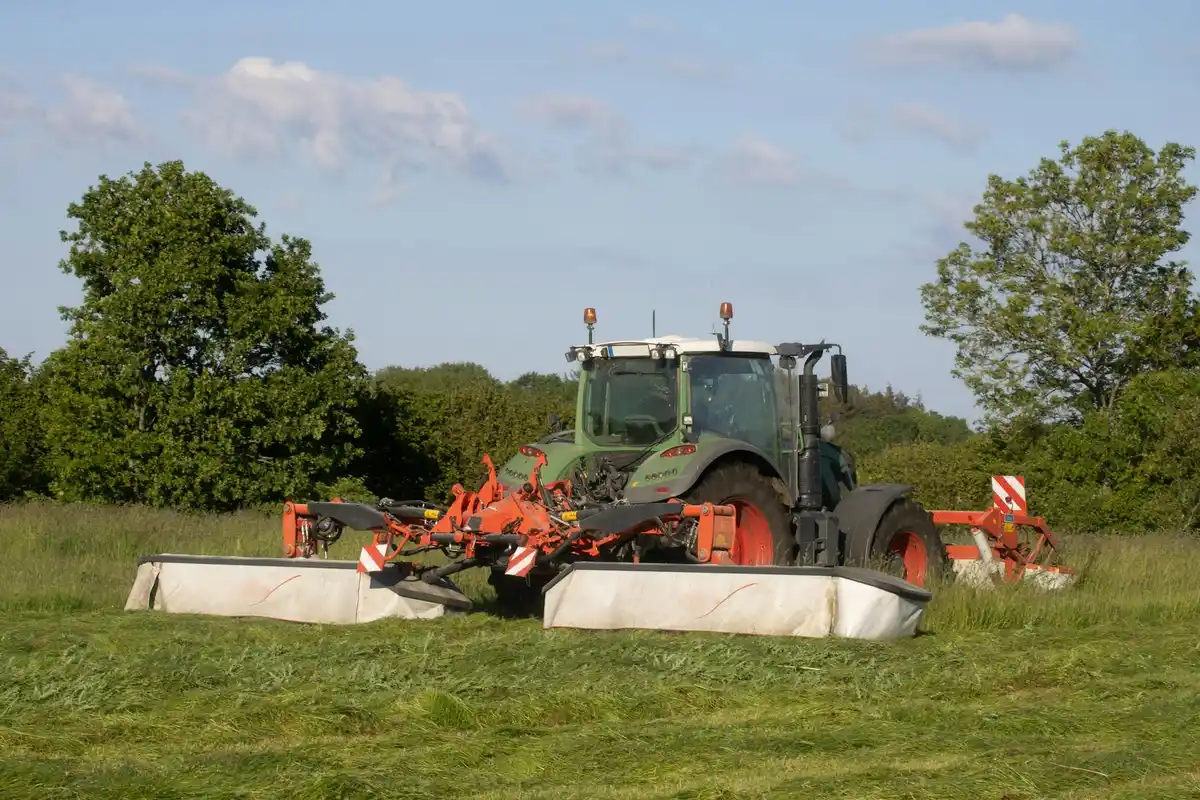 Green and orange lawn tractor with front-mounted mowing attachments in a grassy field under a blue sky