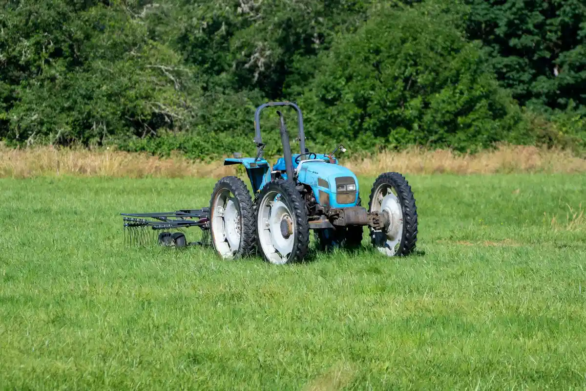 Blue farm tractor in a grassy field with trees in the background