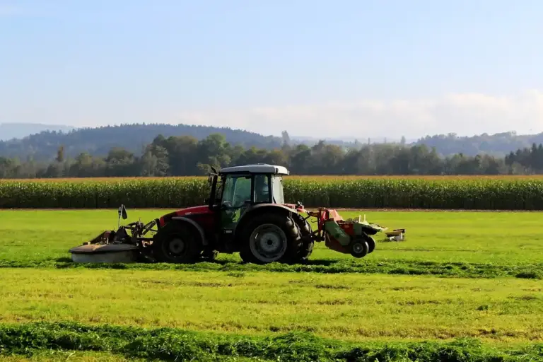 Red tractor with mower attachment working in a green field on a sunny day