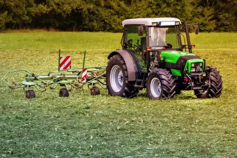 Green tractor with attached agricultural equipment in a grassy field.