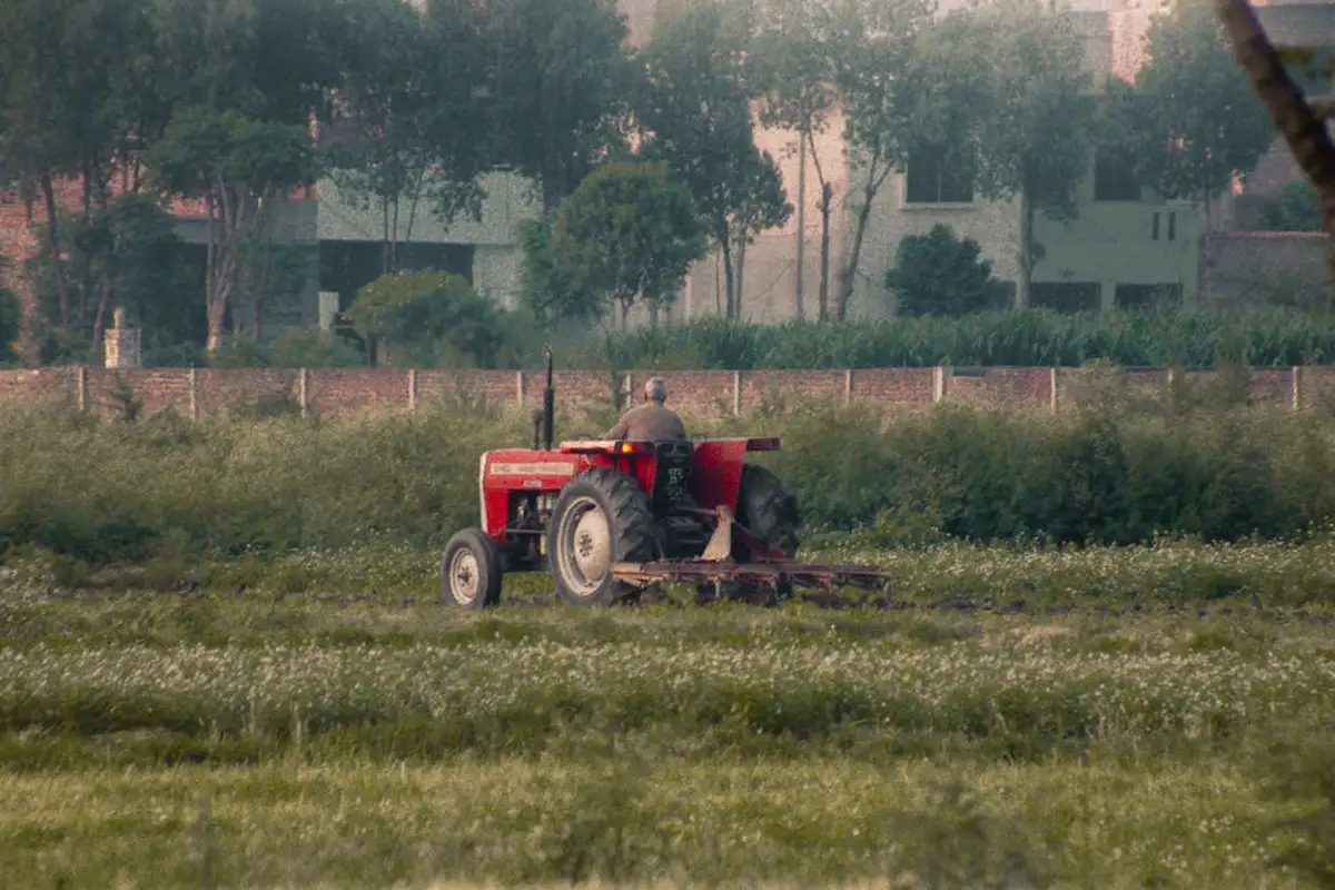 Red tractor with a mower attachment operating in a wide grassy field.