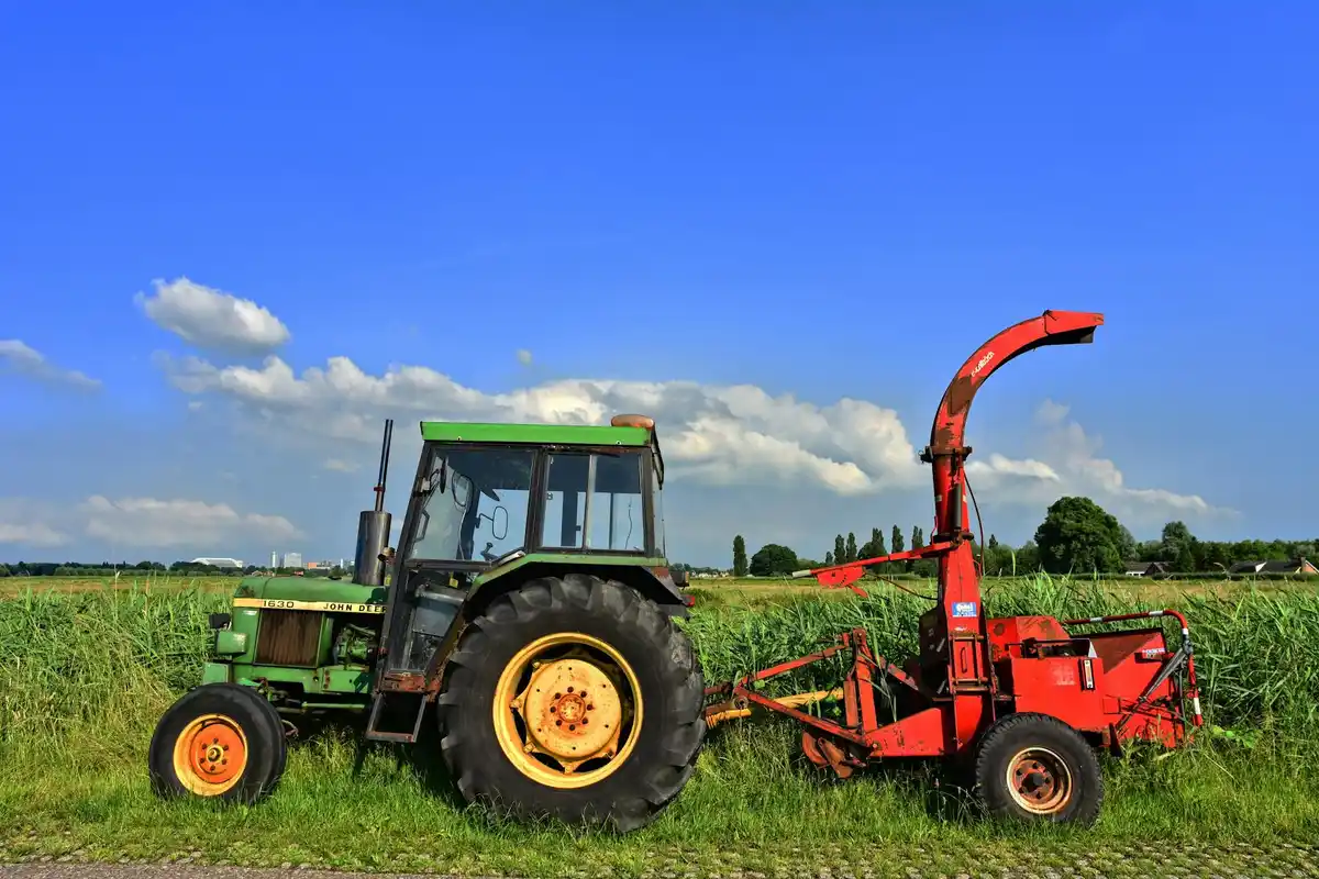 Green tractor with a red lawn mower attachment in a grassy field under a bright blue sky.