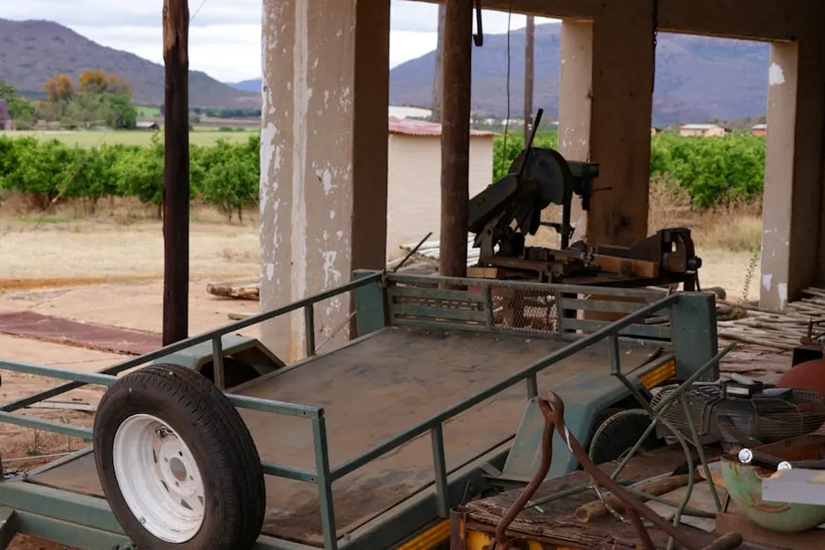 Lawn mower on a trailer under a roofed shelter in a rural setting, ready for winter storage and transport