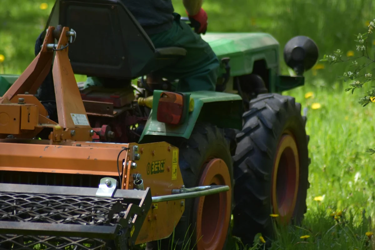 Green rider mower with a front-mounted cutting deck in a grassy field.