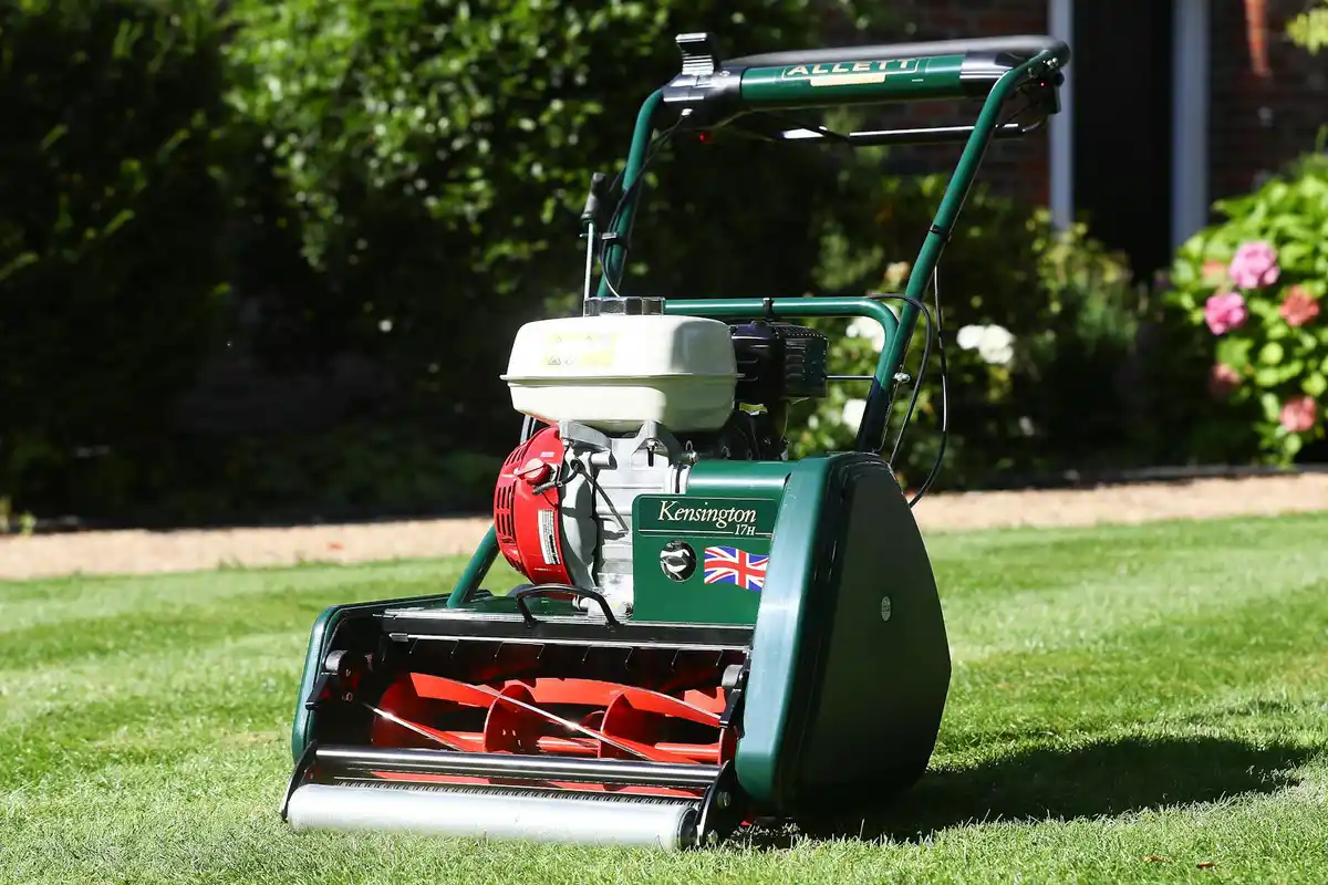 Green lawn roller on a freshly mowed lawn with a house and flowering plants in the background.