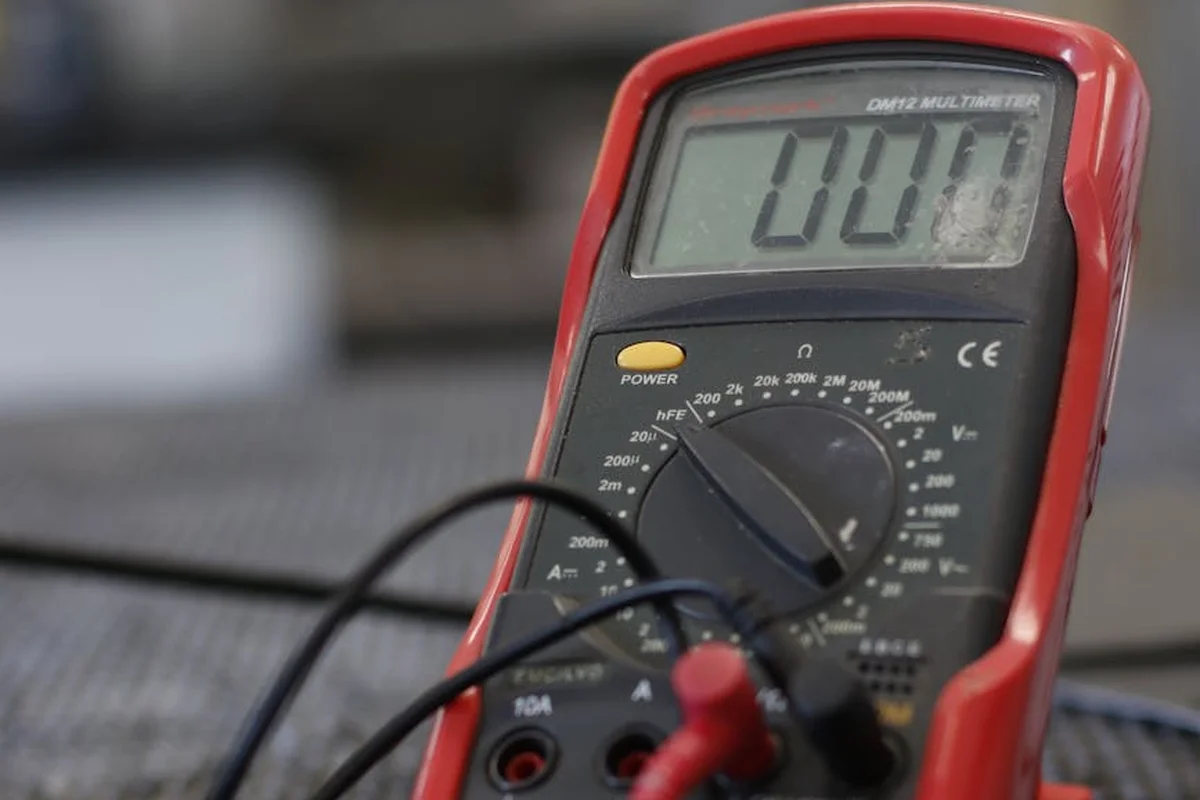 Close-up of a red digital multimeter with probes connected, displaying a reading.